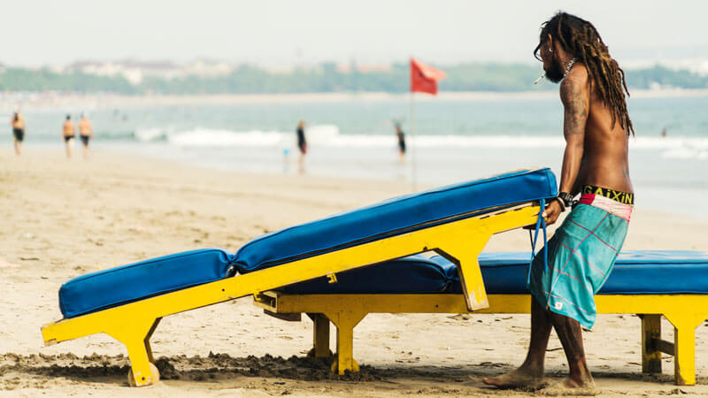 Penjaga pantai Seminyak mengatur daybed di tepi pantai. Panduan Wisata Lengkap ke Seminyak