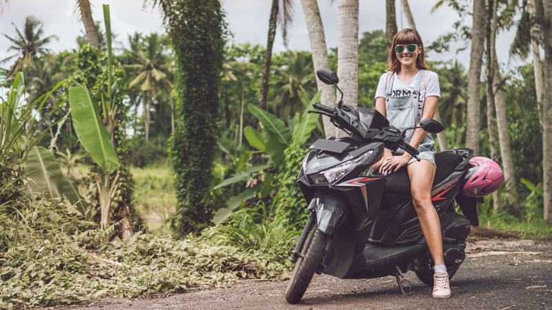 Wisatawan wanita dengan skuter sewaan di jalan pedesaan Bali siap menjelajahi pulau Dewata