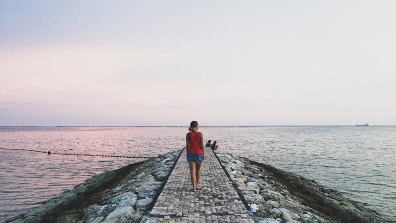 Pengunjung berjalan di tepi Pantai Sanur saat matahari terbit.