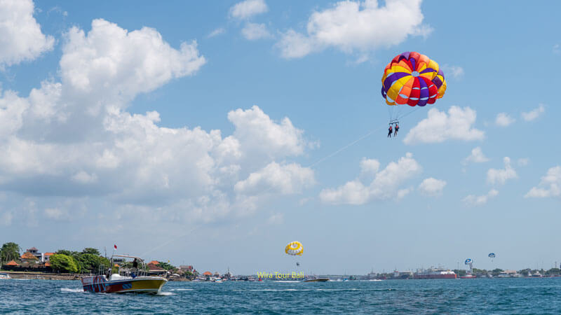 Pengunjung menikmati parasailing di atas laut biru Bali dengan langit cerah