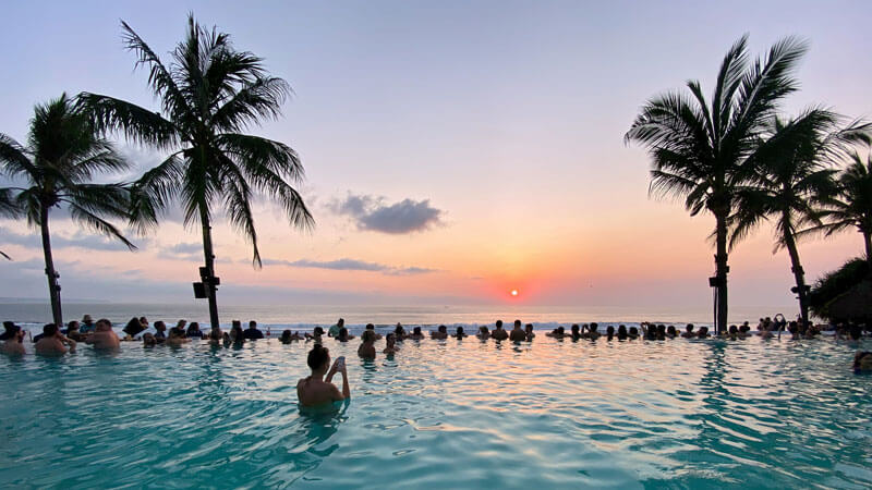 Wisatawan menikmati matahari terbenam di infinity pool dengan pohon palem di Bali