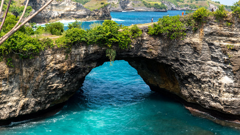 Pantai Pasih Uug Nusa Penida dengan formasi batu alami yang menciptakan jembatan alam di atas lautan biru.