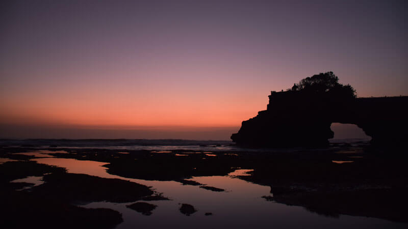 Matahari terbenam yang menakjubkan di Pura Tanah Lot, Bali, dengan langit merah dan siluet pura di latar depan.