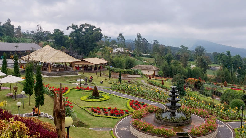 Taman bunga indah dengan air mancur di tengah-tengah, gazebo beratap jerami, dan jalan setapak di The Blooms Garden Bedugul.