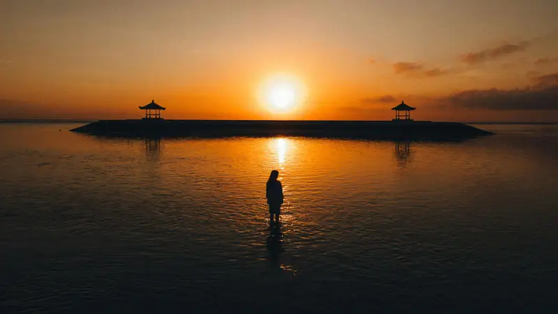 Sunrise di Pantai Sanur dengan siluet bale tradisional di tepi laut.