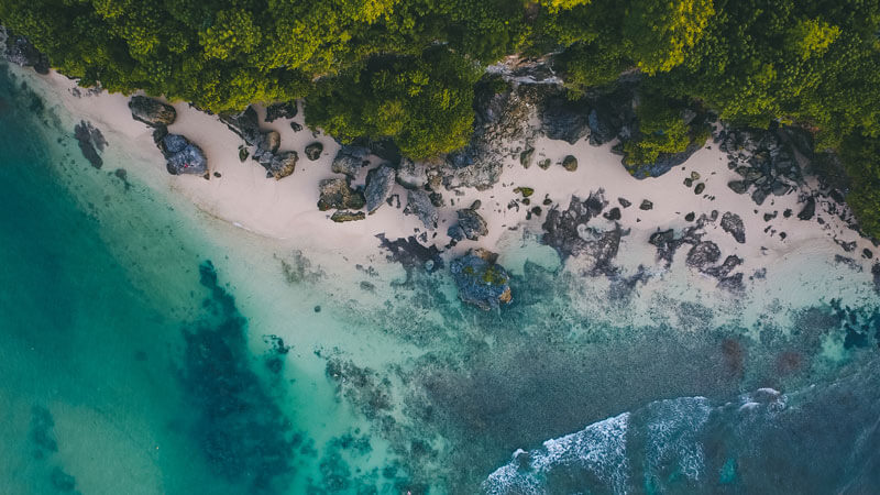 Pemandangan atas Pantai Padang Padang di Bali, menampilkan pasir putih, batuan hitam, dan air jernih