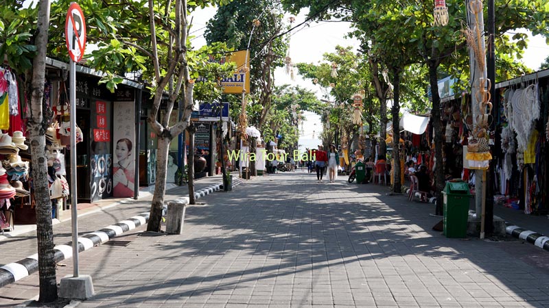 Jalan utama pasar seni di Tanah Lot, Bali, dengan deretan toko suvenir dan pohon-pohon rindang.