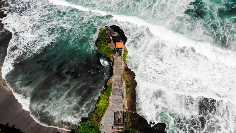 Pemandangan udara Pura Tanah Lot yang terpisah dari daratan oleh ombak laut yang berbuih di Bali.