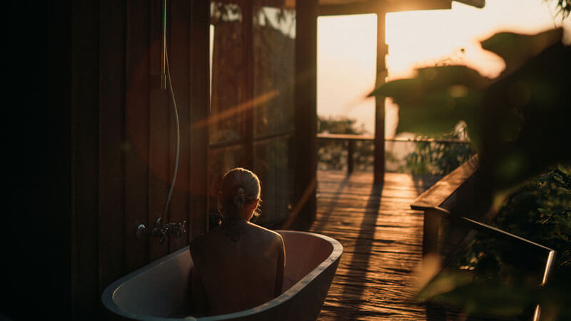 Seorang wanita yang sedang bersantai di bathtub di luar ruangan dengan pemandangan matahari terbenam di Bali Utara