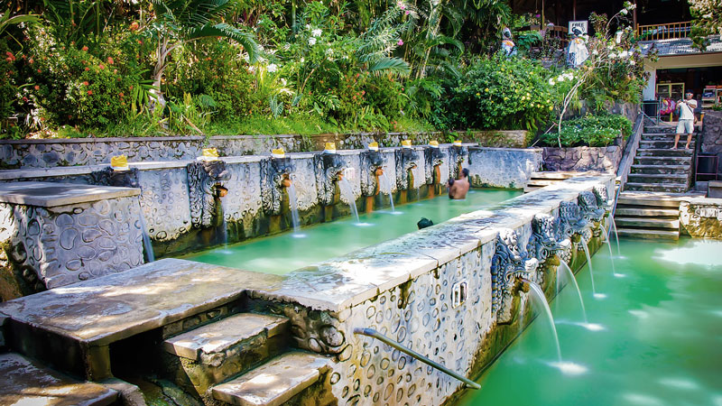 Pemandangan kolam air panas Banjar dengan pengunjung yang sedang berendam di air kaya mineral di Bali Utara