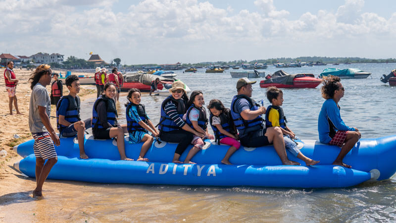 Keluarga sedang menikmati permainan banana boat di tepi pantai Bali yang cerah