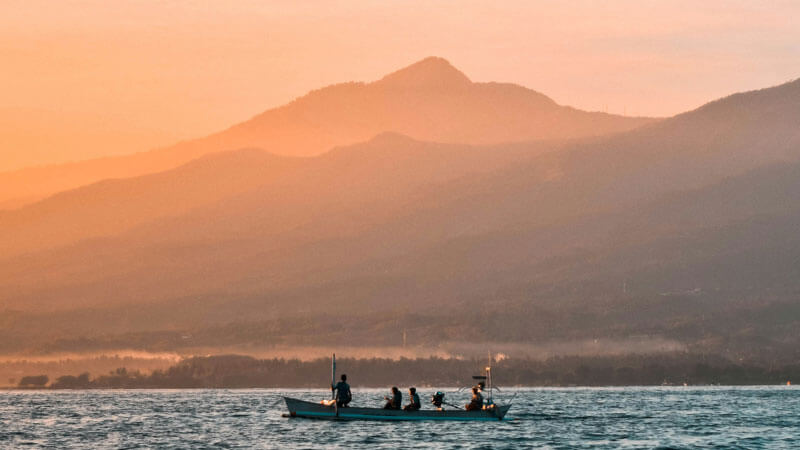 Para nelayan di perahu tradisional dengan latar belakang cahaya fajar dan gunung di Bali Utara