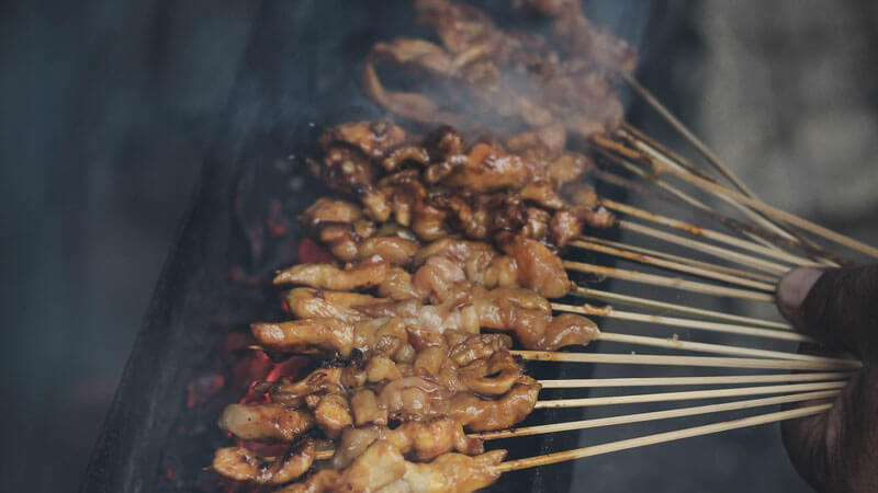 Sate lilit khas Bali sedang dibakar, aroma rempah yang menggoda menguar dari warung kaki lima di Bali Utara