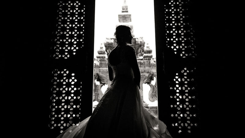 Siluet mempesona pengantin wanita menghadap Monumen Bajra Sandhi, melalui celah-celah pintu tradisional Bali.