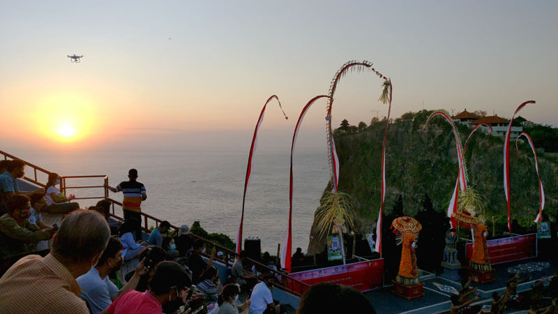 Penonton menyaksikan pertunjukan Tari Kecak pada saat senja di Pura Uluwatu dengan latar belakang matahari terbenam dan Samudra Hindia.