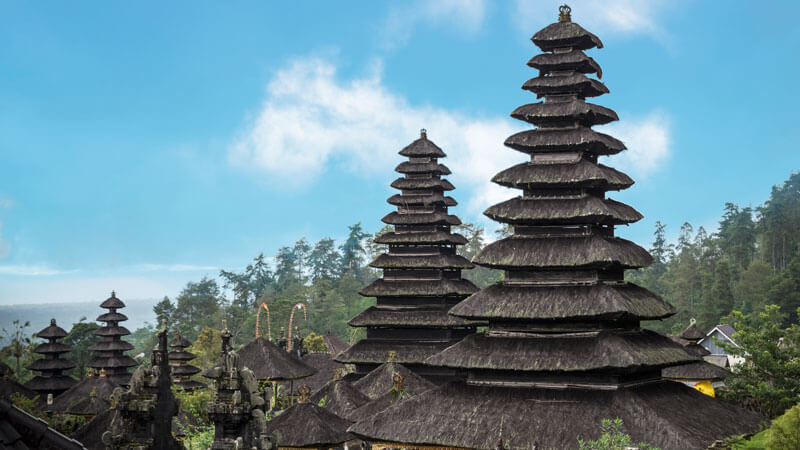 Menara-menara Meru yang bertingkat di Pura Besakih dengan latar belakang hutan dan langit biru