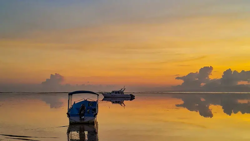 Matahari terbit di Pantai Sanur dengan perahu tradisional Bali.