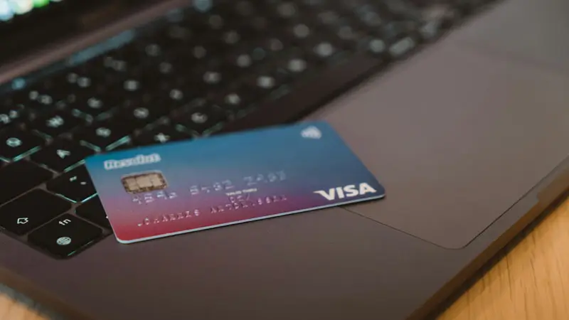 Kartu Visa terletak di atas keyboard laptop, siap untuk transaksi pembayaran online, Syarat dan Ketentuan Paket Tour Bali