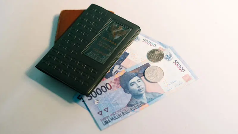 Uang kertas dan koin rupiah di samping dompet dan paspor