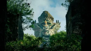 Patung Garuda Wisnu Kencana Bali yang megah, dikelilingi pepohonan dan diapit tebing batu, menciptakan pemandangan dramatis di GWK Cultural Park.