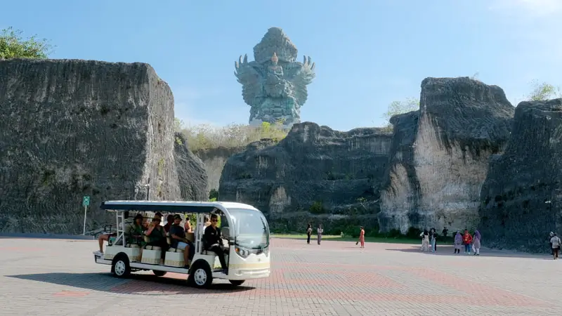Wisatawan menaiki shuttle buggy dengan latar belakang Patung, memudahkan perjalanan keliling taman budaya. Foto © Garuda Wisnu Kencana