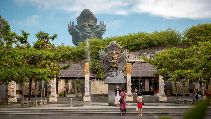 Pintu masuk Garuda Wisnu Kencana Bali dengan patung Garuda Wisnu raksasa di latar belakang, menampilkan area taman budaya yang hijau dan asri. Foto © GWK