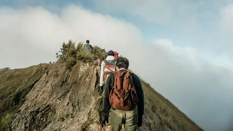 Pendaki menyusuri lereng sempit berbatu dalam kabut pagi