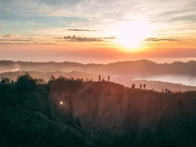 Matahari terbit dari puncak Gunung Batur dengan siluet pendaki di tepi kawah