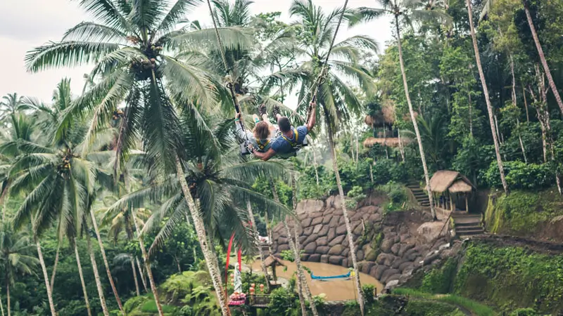 Pasangan honeymoon naik Bali Swing tandem dengan latar lembah hijau dan pohon kelapa