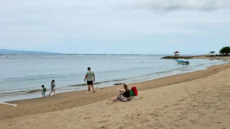 Keluarga bermain di tepi Pantai Sanur dengan pasir lembut dan laut yang tenang