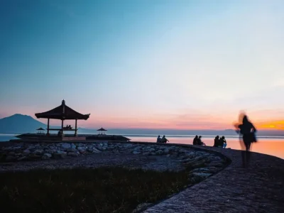 Wisata sunrise di Pantai Sanur Denpasar dengan gazebo dan beberapa pengunjung di tepi laut tenang