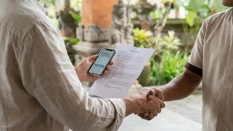 Ilustrasi jabat tangan saat konfirmasi itinerary sebelum deposit, layar HP dan kertas diblur.