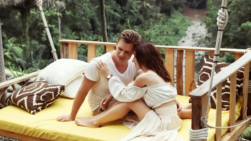 Pasangan duduk di daybed dengan pemandangan lembah hijau